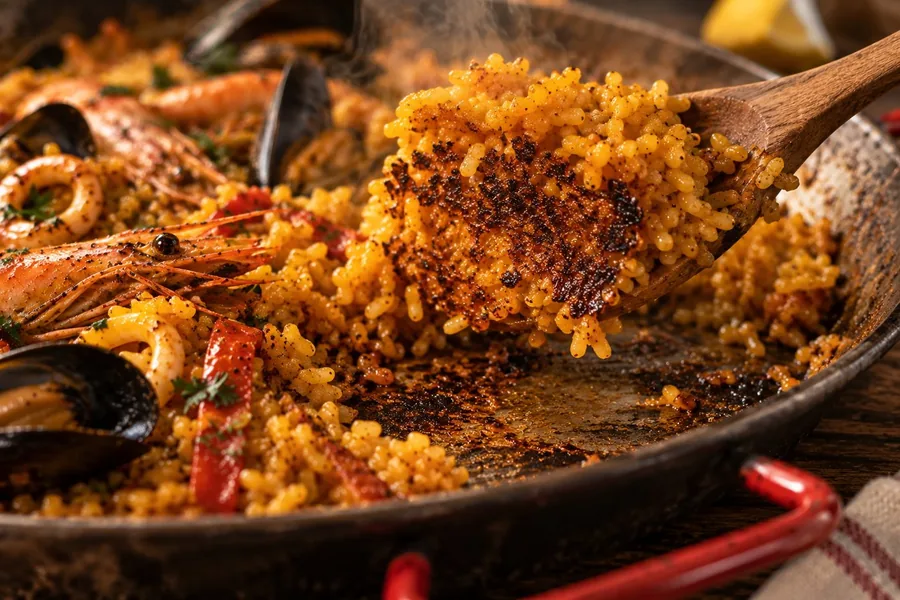 Cuchara levantando arroz del fondo de la paellera, con el socarrat tostado a la vista